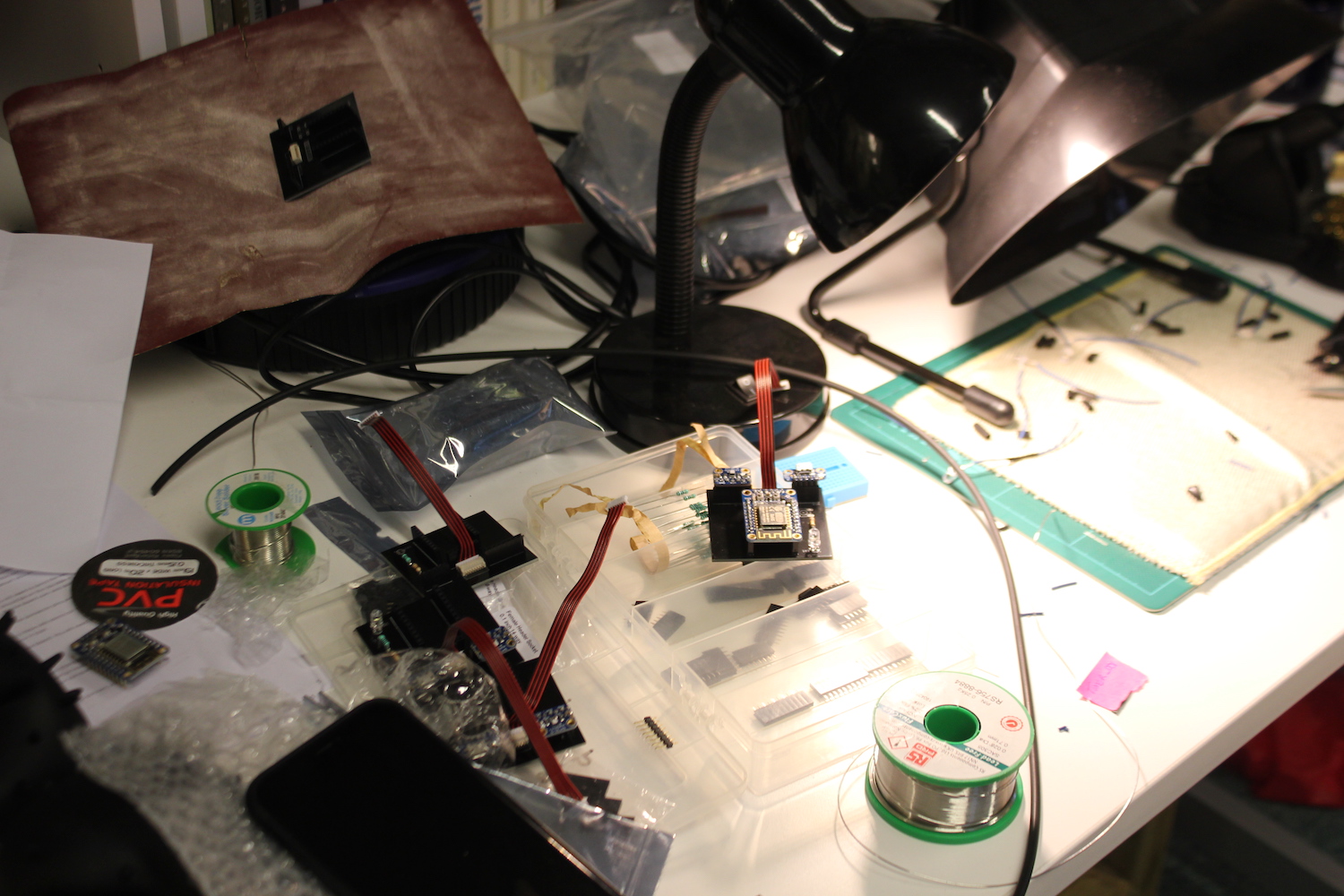 A view of the desk used for soldering in the Citizen Sense lab showing part assembled Dustboxes, extractor fan, solder, light and heatproof mat