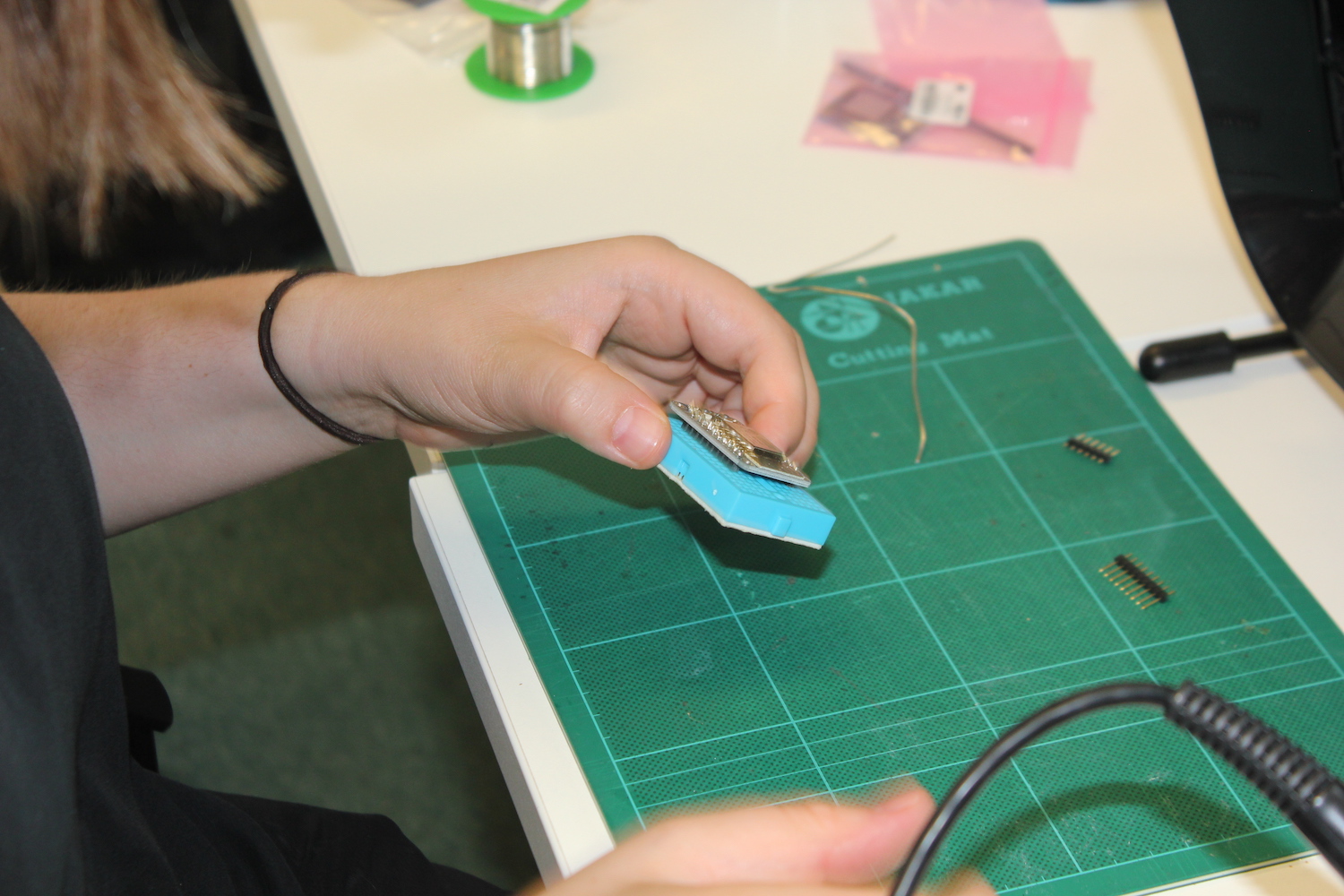 A researcher holds a small breadboard containing the Adafruit Huzzah ESP8266 Breakout to pin headers in one hand as she prepares to solder