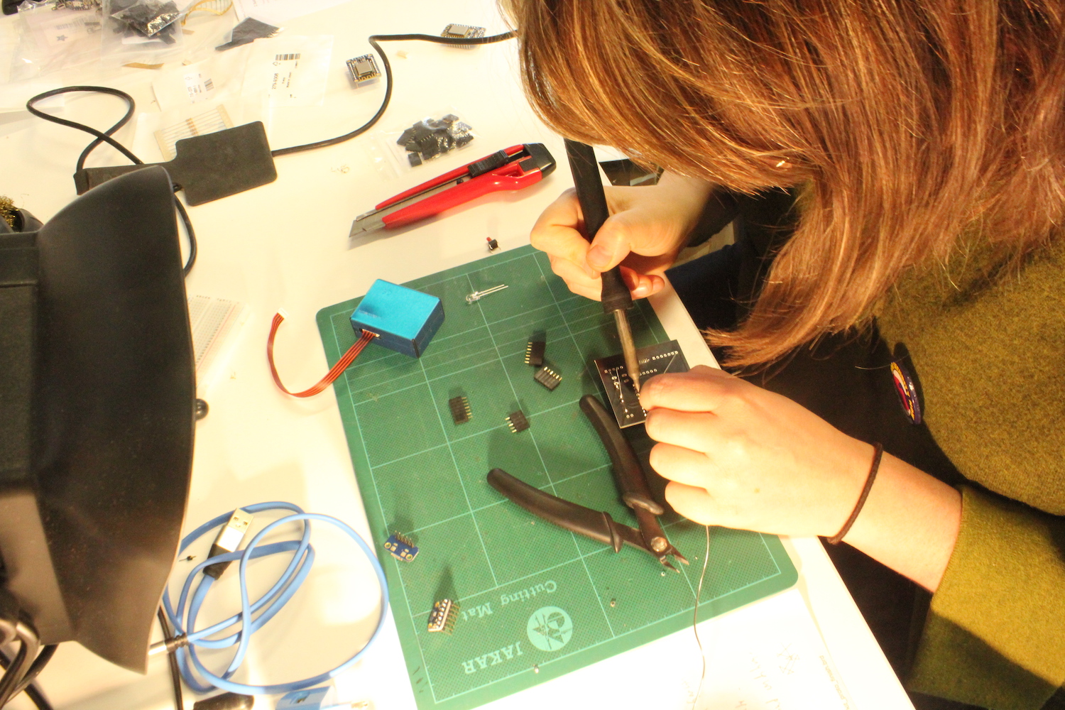 A researcher holds a soldering iron in her hand as she solders parts to the Dustbox 2.0 PCB