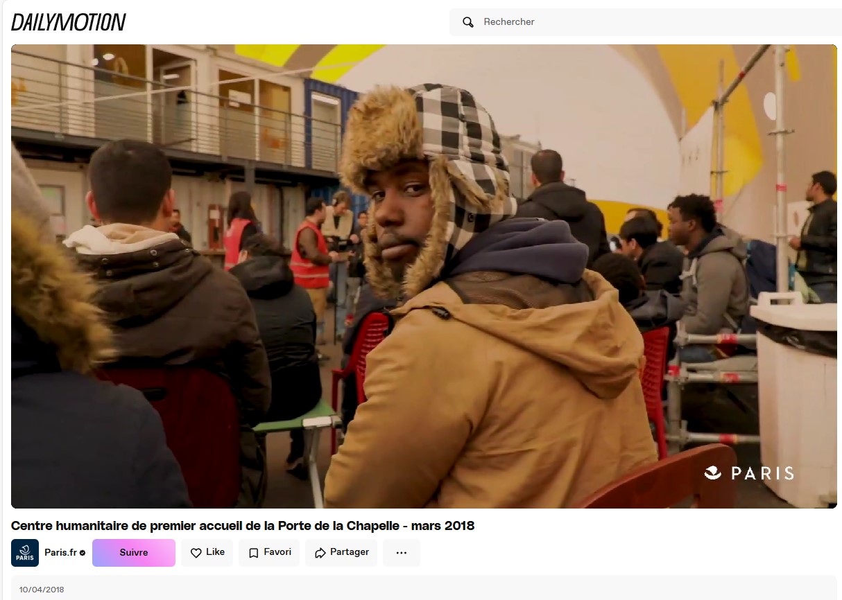 Vidéo publié par Paris.fr le 10/04/2018 sur Dailymotion, capture d’écran effectué le 8/04/2025 Dans la vidéo de communication de la Ville de Paris, on parle de 2015 avec « l’apparition des premiers campements de réfugiés dans les rues de Paris », puis en 2016, l’ouverture du Centre humanitaire de Premier Accueil. Sur cet extrait d’image, certains hébergés sont rassemblés pour une réunion d’information dans la bulle d’accueil.